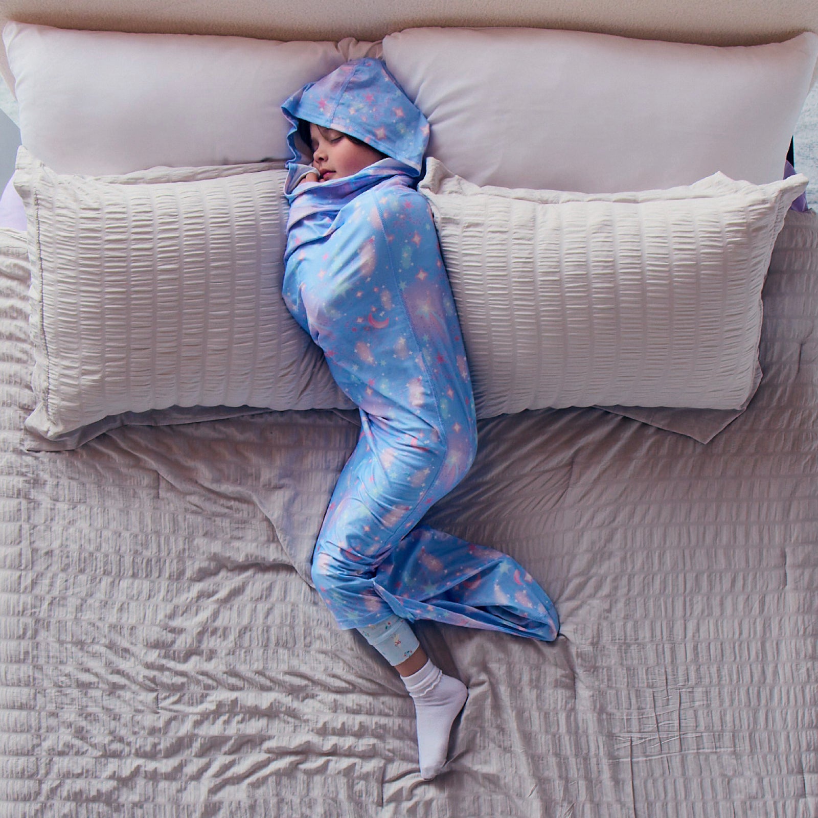 Child sleeping on a bed in a blue star-patterned hooded Sleep Pod.