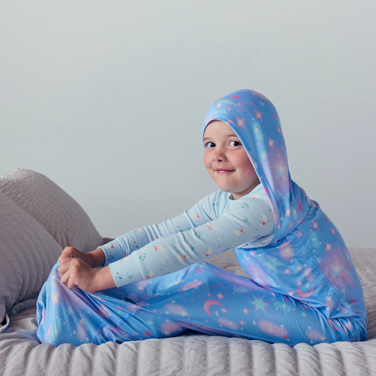 Child sleeping on a bed in a blue star-patterned hooded Sleep Pod.